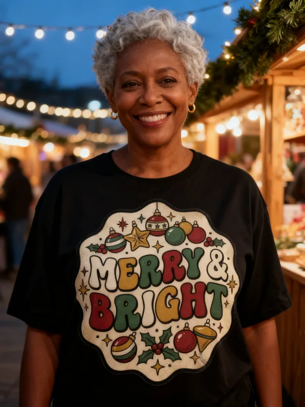 Woman at an outdoor Christmas market at dusk wearing the Merry & Bright Christmas tee
